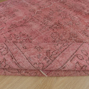 May include: A rolled-up, distressed pink rug with a faded floral pattern. The rug features dark brown and white accents, creating a vintage aesthetic. The rug is made of a woven material.
