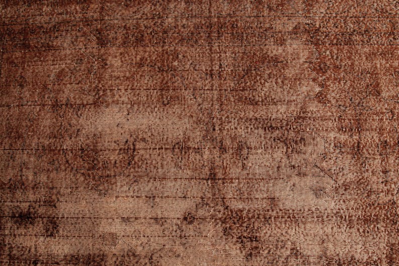 May include: A woven textile surface featuring a deep brown and copper color palette. The fabric displays a distressed, weathered appearance with visible horizontal and vertical thread patterns, creating a textured, mottled, and uneven visual effect.