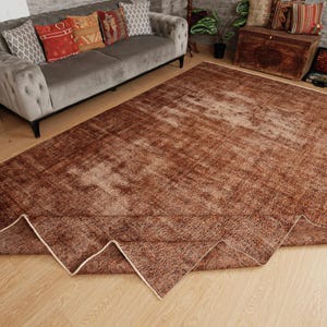 May include: A large rectangular area rug featuring a distressed, weathered texture in shades of deep brown and copper. The rug has a faded, mottled appearance with a visible folded corner revealing a light-colored edge binding on the underside.