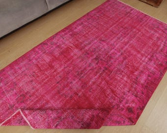 May include: A rectangular area rug featuring a vibrant fuchsia and magenta colour palette with a distressed, weathered texture. The rug displays a faded, intricate pattern throughout its surface, with one corner folded over to reveal the underside.