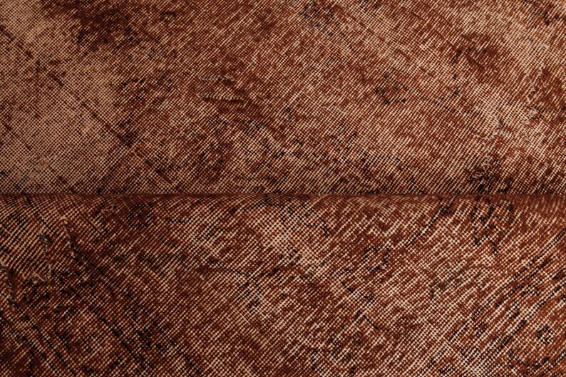 May include: A piece of fabric featuring a deep rust-brown color with a distressed, weathered texture. The material displays a diagonal weave pattern with darker, mottled patches that create a worn appearance across the entire surface area.