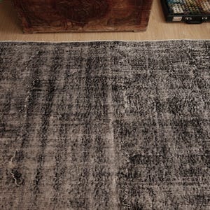 May include: A rectangular area rug featuring a distressed, mottled pattern in shades of charcoal grey and black. The woven textile displays a faded, weathered appearance with visible variations in colour density across the surface.