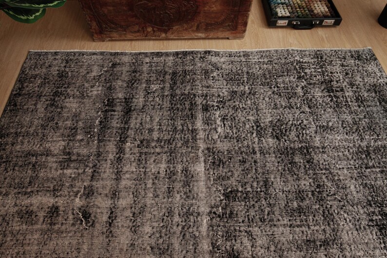 May include: A rectangular area rug featuring a distressed, mottled pattern in shades of charcoal grey and black. The woven textile displays a faded, weathered appearance with visible variations in colour density across the surface.