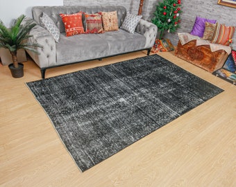 Pode incluir: Um tapete preto e branco desgastado com um visual desbotado e vintage. O tapete está colocado sobre um piso de madeira clara na frente de um sofá cinza com almofadas.