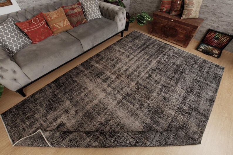 May include: A large rectangular area rug featuring a distressed, mottled pattern in shades of charcoal grey, black, and faded white. The rug has a low-pile texture with a worn, vintage-inspired appearance and a finished edge binding.