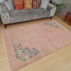 May include: A light pink vintage rug with a floral design. The rug has a faded, distressed look and features a floral pattern in shades of green, pink, and yellow.