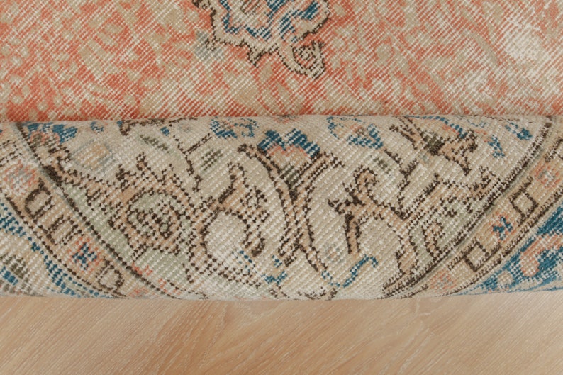 Puede incluir: Primer plano de una alfombra enrollada con fondo beige y dise&ntilde;o estampado en azul, marr&oacute;n y blanco.