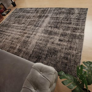 May include: A rectangular area rug featuring a distressed, mottled pattern in shades of charcoal grey, black, and faded white. The rug has a low-pile texture with visible variations in colour density, creating a weathered, aged appearance across the surface.