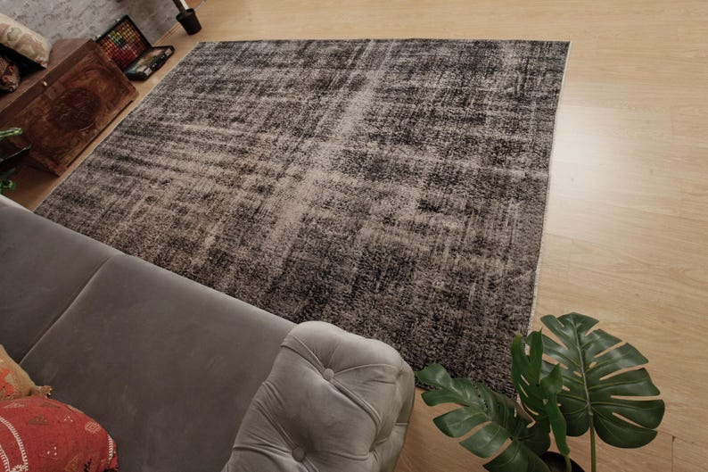 May include: A rectangular area rug featuring a distressed, mottled pattern in shades of charcoal grey, black, and faded white. The rug has a low-pile texture with visible variations in colour density, creating a weathered, aged appearance across the surface.