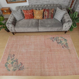May include: A light pink vintage rug with a floral design. The rug has a distressed look and features a faded floral pattern in the corners.