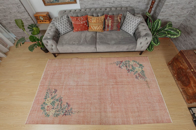 May include: A light pink vintage rug with a floral design. The rug has a distressed look and features a faded floral pattern in the corners.