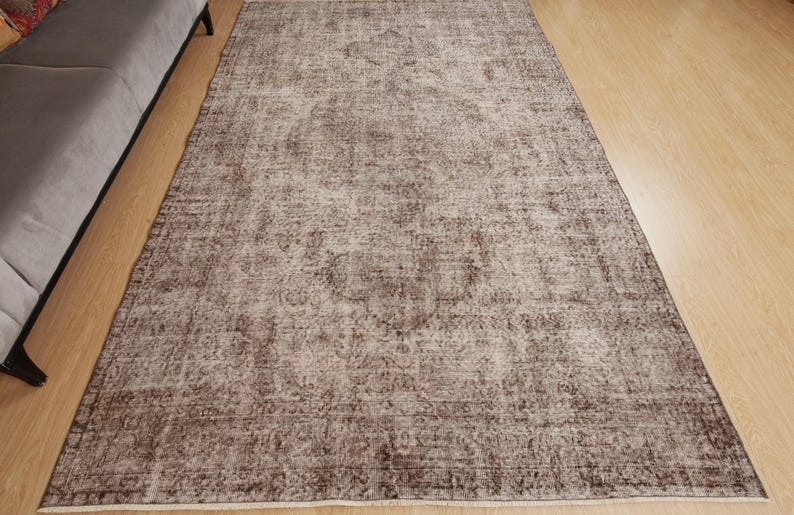 May include: A rectangular, distressed-look rug with a faded, vintage appearance. The rug features a central medallion design and a border, with a color palette of brown and cream. The rug is placed on a hardwood floor.