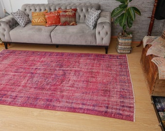May include: A vintage pink and purple area rug with a faded floral pattern. The rug is laid out on a wooden floor in a living room setting.