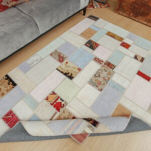 Może przedstawiać: Dywan patchworkowy z różnymi kolorami i wzorami, w tym beżowym, białym, niebieskim i czerwonym. Dywan jest wykonany z różnych kawałków tkaniny zszytych ze sobą, tworząc unikalny i eklektyczny wzór.