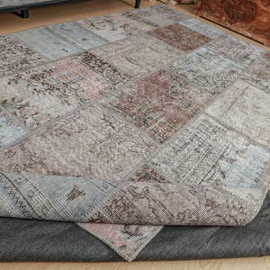 Puede incluir: Una alfombra de patchwork con una variedad de colores y patrones. La alfombra está hecha de diferentes piezas de tela cosidas juntas. La alfombra está doblada por la mitad y se ve el revés.
