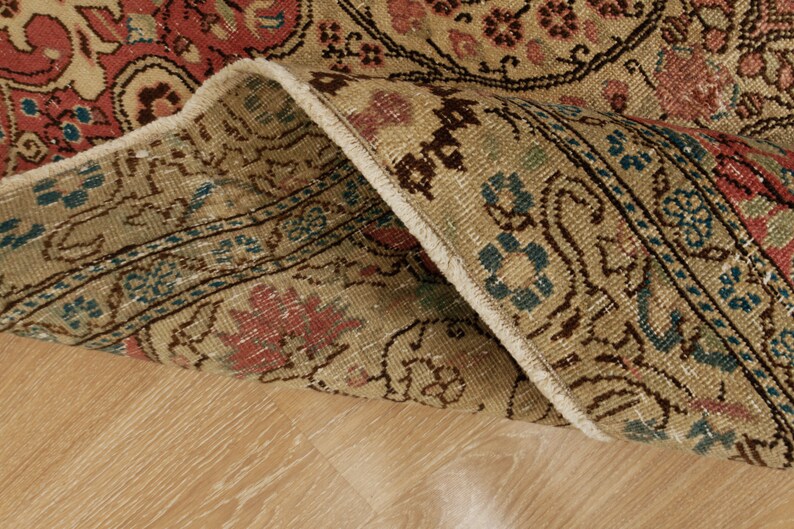 Pu&ograve; includere: Primo piano di una sezione di un tappeto vintage con un bordo piegato. Il tappeto presenta uno sfondo beige con intricati motivi floreali in rosso, blu e marrone. La trama e il design suggeriscono che si tratti di un oggetto d'antiquariato o di una riproduzione di alta qualit&agrave;.
