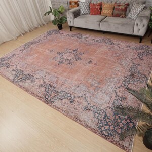 May include: A large rectangular area rug featuring a faded terracotta orange center with a dark blue floral medallion. The border displays intricate dark blue and muted grey floral patterns against a light terracotta background, creating a distressed look.