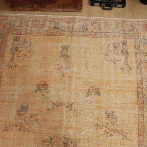 May include: A vintage rug with a beige background and a floral pattern in shades of brown, orange, and gray. The rug has a faded look and a worn texture.