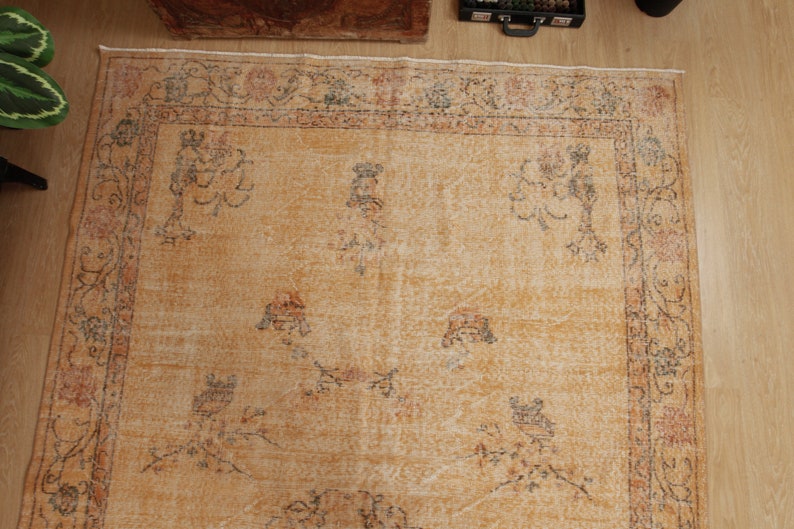 May include: A vintage rug with a beige background and a floral pattern in shades of brown, orange, and gray. The rug has a faded look and a worn texture.