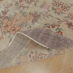 May include: A beige rug with a floral pattern in shades of brown, pink, and green. The rug is folded in half, showing the underside, which is a darker beige color.