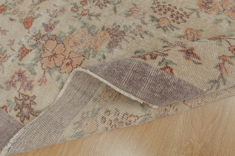 May include: A beige rug with a floral pattern in shades of brown, pink, and green. The rug is folded in half, showing the underside, which is a darker beige color.