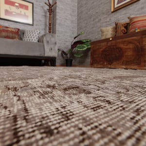 May include: A low-angle shot of a patterned rug in a room with a gray sofa, wooden chest, and framed artwork. The rug has a beige and brown design, with a textured appearance. The room has a neutral color palette, creating a cozy atmosphere.
