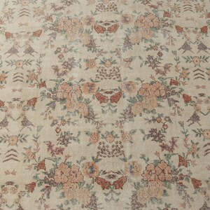 May include: A vintage rug with a cream background and a floral pattern in shades of pink, brown, and green. The rug has a brown border.