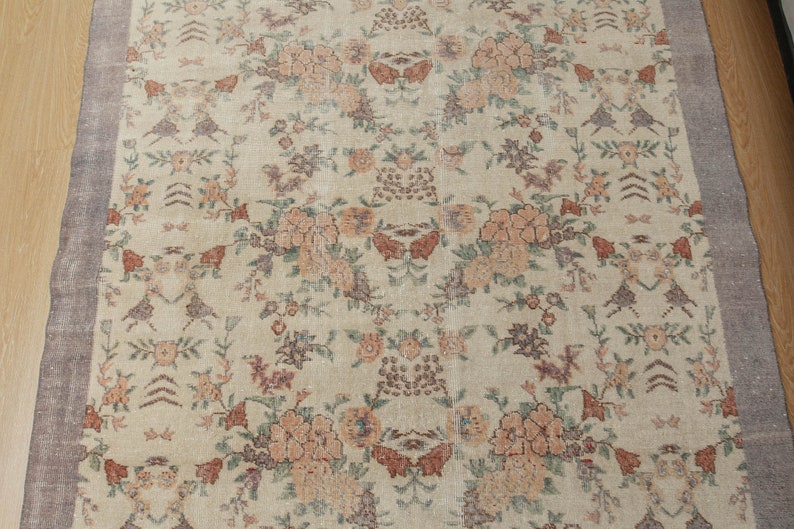 May include: A vintage rug with a cream background and a floral pattern in shades of pink, brown, and green. The rug has a brown border.