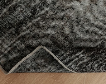 Pode incluir: Close-up de um tapete preto e branco com um visual desgastado e vintage. O tapete está dobrado, mostrando o avesso do tecido.