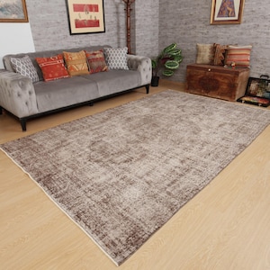 May include: A large, rectangular, distressed-look rug in shades of brown and beige dominates the room. The rug has a faded, vintage appearance, with a central pattern and a lighter border. The rug is placed on a light-colored wooden floor.