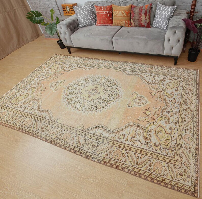 May include: A large, rectangular, vintage-style rug with an intricate floral pattern in shades of peach, cream, and brown. The rug features a central medallion design and a detailed border. The rug is placed on a light-colored wooden floor.
