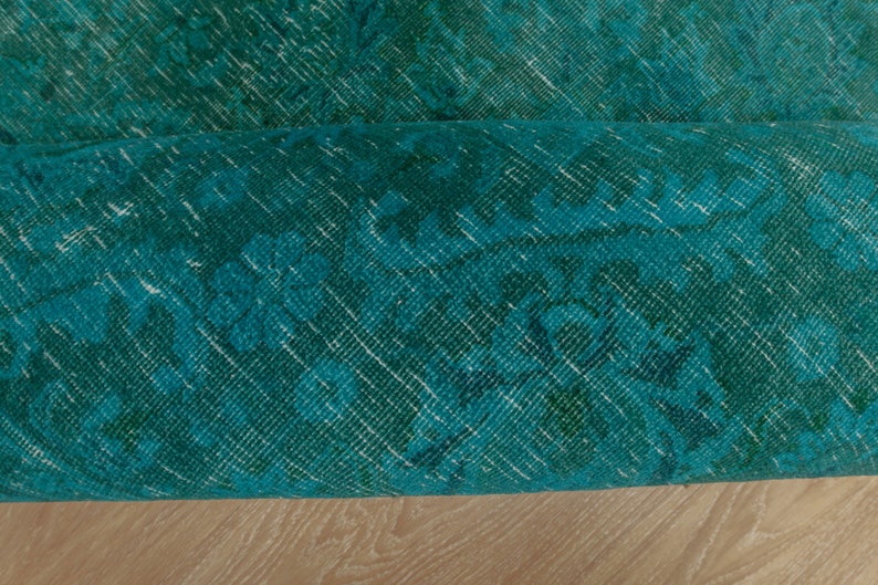 May include: Close-up of a teal blue rug with a faded floral pattern. The rug is rolled up and the edge is visible.