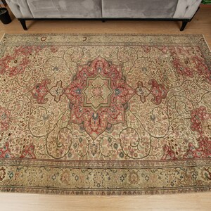 Pu&ograve; includere: Un tappeto rettangolare con un intricato disegno floreale. Il tappeto ha una base color crema con un medaglione centrale rosso e blu. Il motivo dettagliato include elementi floreali in rosso, blu e verde. Il bordo &egrave; verde scuro.