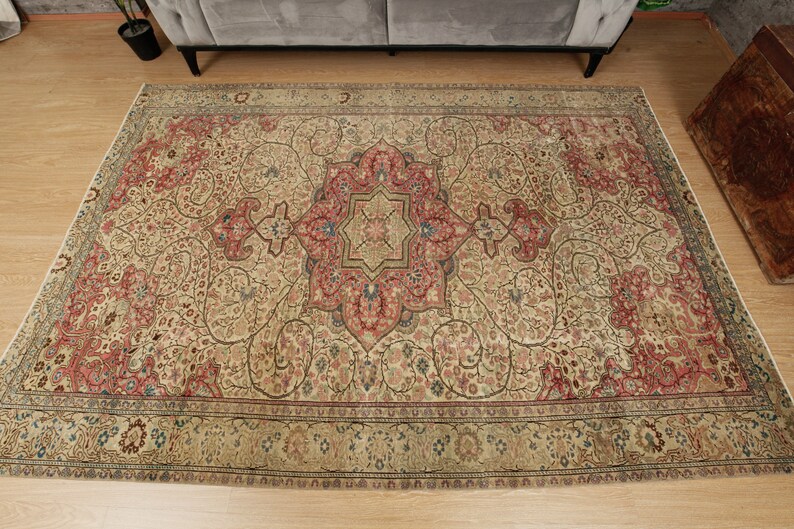 Pu&ograve; includere: Un tappeto rettangolare con un intricato disegno floreale. Il tappeto ha una base color crema con un medaglione centrale rosso e blu. Il motivo dettagliato include elementi floreali in rosso, blu e verde. Il bordo &egrave; verde scuro.