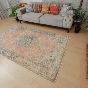 Puede incluir: Una alfombra de estilo vintage con un esquema de color descolorido en melocot&oacute;n, azul y crema. La alfombra tiene un patr&oacute;n floral y un aspecto desgastado.