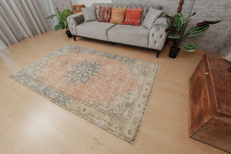 Puede incluir: Una alfombra de estilo vintage con un esquema de color descolorido en melocot&oacute;n, azul y crema. La alfombra tiene un patr&oacute;n floral y un aspecto desgastado.