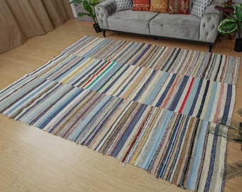 May include: A large, rectangular rug with a patchwork design. The rug features a variety of vertical stripes in shades of blue, beige, red, and green. The rug is made of a woven material and is placed on a wooden floor.