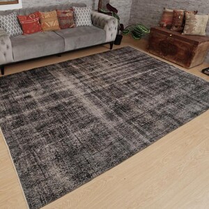 May include: A large rectangular area rug featuring a distressed, weathered appearance with a dark charcoal and black colour palette. The rug displays a faded, mottled texture with subtle variations in tone across its surface, laid flat.