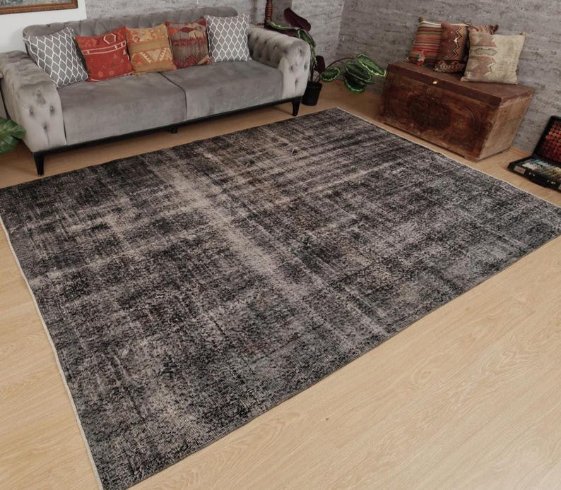 May include: A large rectangular area rug featuring a distressed, weathered appearance with a dark charcoal and black colour palette. The rug displays a faded, mottled texture with subtle variations in tone across its surface, laid flat.