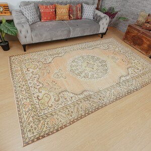 May include: A large, rectangular area rug with an intricate, traditional design. The rug features a central medallion and ornate borders in shades of peach, cream, and brown. The rug is placed on a light-colored wooden floor.