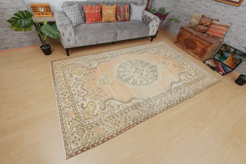 May include: A large, rectangular area rug with an intricate, traditional design. The rug features a central medallion and ornate borders in shades of peach, cream, and brown. The rug is placed on a light-colored wooden floor.