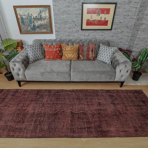 May include: A dark brown area rug with a distressed, vintage look. The rug is laid out on a wooden floor in front of a grey sofa with cushions.