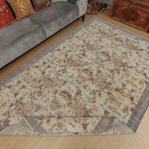 May include: A cream-colored rug with a floral pattern in shades of brown, pink, and green. The rug has a gray border and is rolled up on one side.