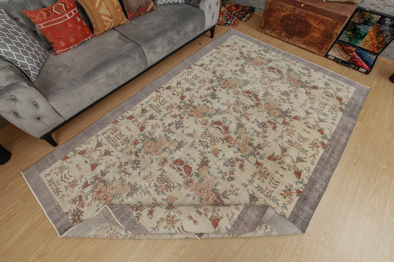 May include: A cream-colored rug with a floral pattern in shades of brown, pink, and green. The rug has a gray border and is rolled up on one side.