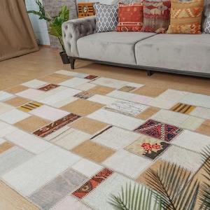 Może przedstawiać: Biało-beżowy dywan patchworkowy z różnymi kolorami i wzorami. Dywan wykonany jest z różnych tkanin i faktur, tworząc unikalny i eklektyczny wygląd.