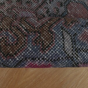 Puede incluir: Primer plano de una alfombra enrollada con un patrón geométrico azul, marrón y rosa.