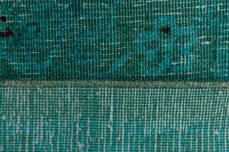 May include: Close-up of a teal blue woven rug with a fringe border. The rug has a textured surface and a subtle pattern.