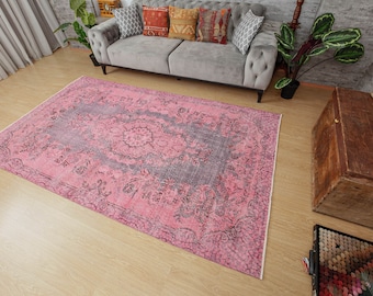 May include: A pink and gray vintage rug with a floral pattern. The rug is laid out on a wooden floor in a living room setting.