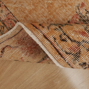 May include: Close-up of the edge of a tan and brown rug with a white fringe. The rug has a geometric pattern in black and red.