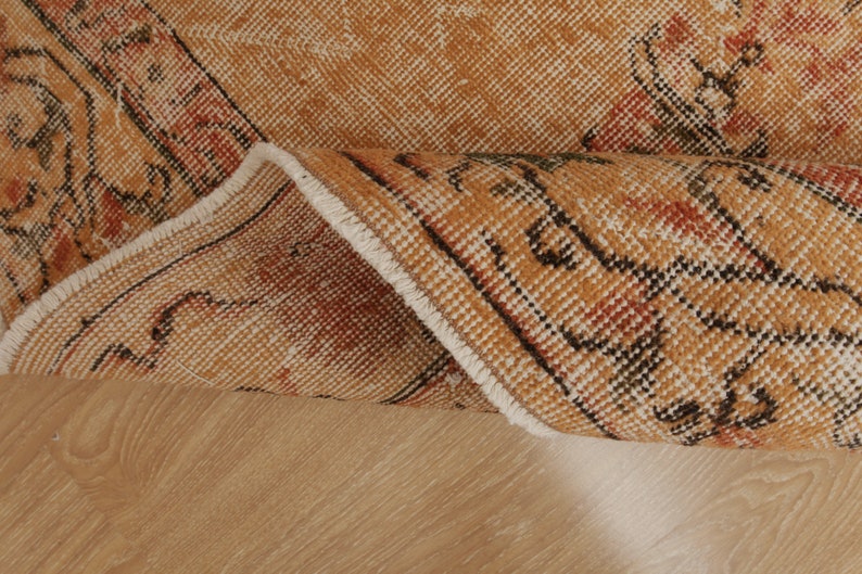 May include: Close-up of the edge of a tan and brown rug with a white fringe. The rug has a geometric pattern in black and red.